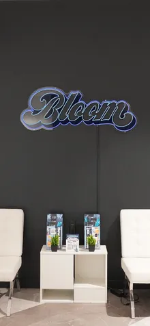 Waiting area at Bloom Athens with white lounge chairs beneath a blue neon Bloom sign.