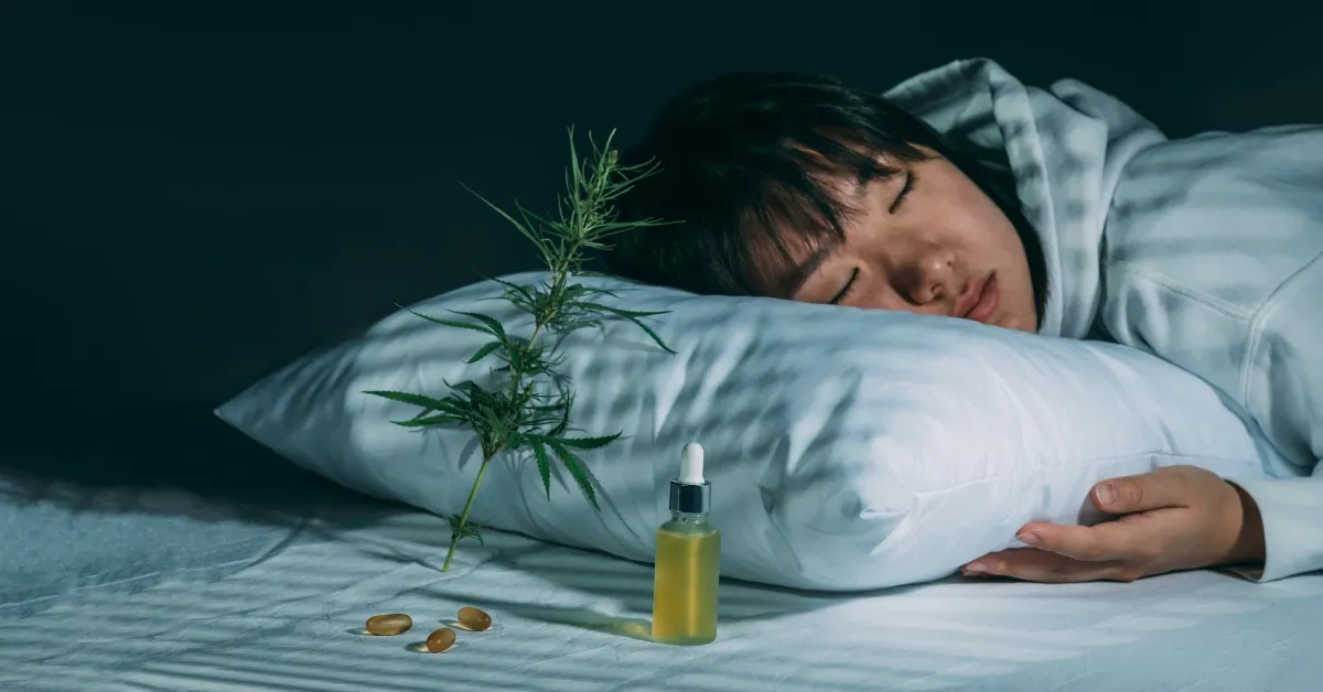 Person sleeping in a dim bedroom beside a cannabis tincture bottle and a cannabis leaf