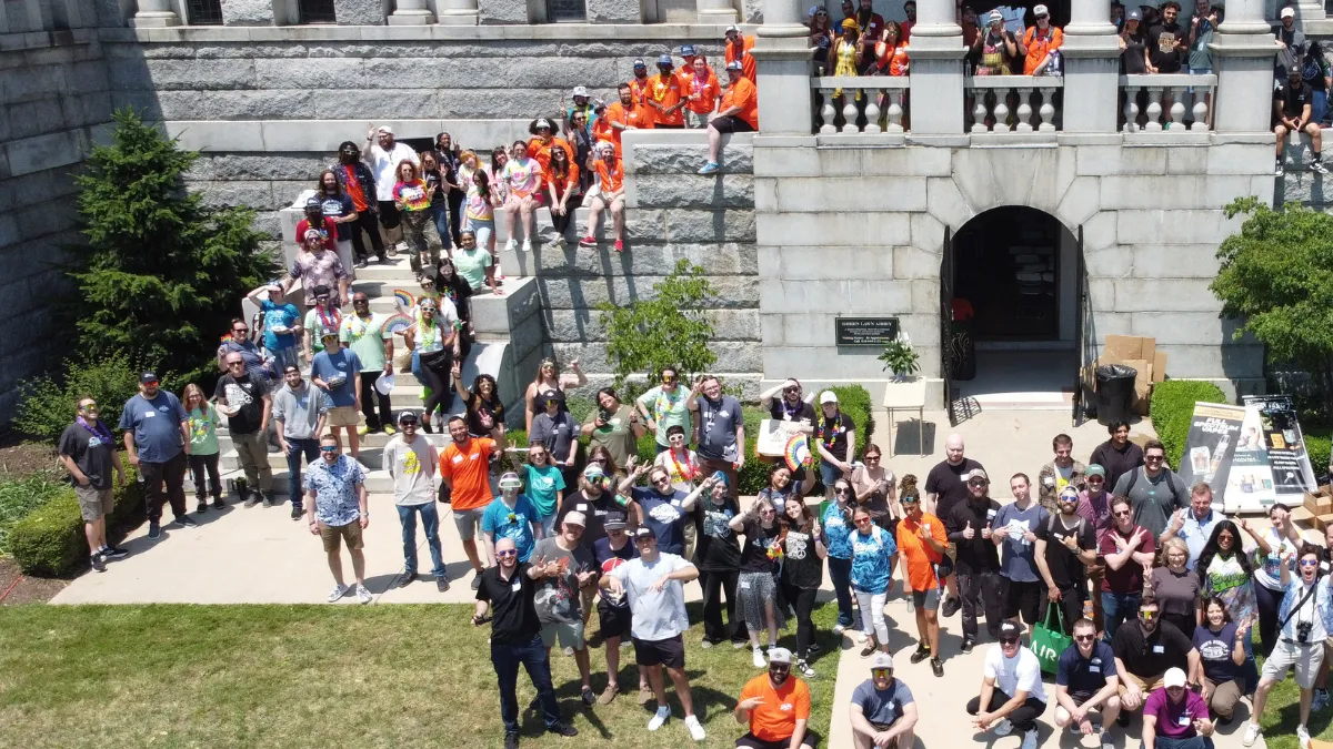 Large group of Bloom Cannabis dispensary team members gathered on the steps and lawn of a stone building, smiling and waving at the camera.