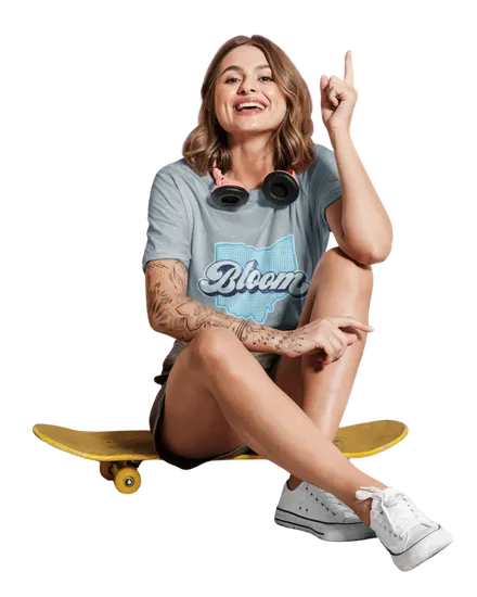 Smiling woman in a Bloom Cannabis Ohio T-shirt sitting on a yellow skateboard and pointing up.