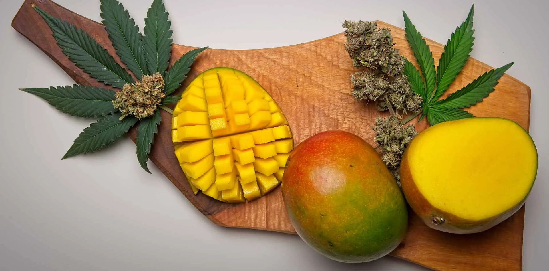 Sliced mangoes beside cannabis buds and leaves on a wooden board