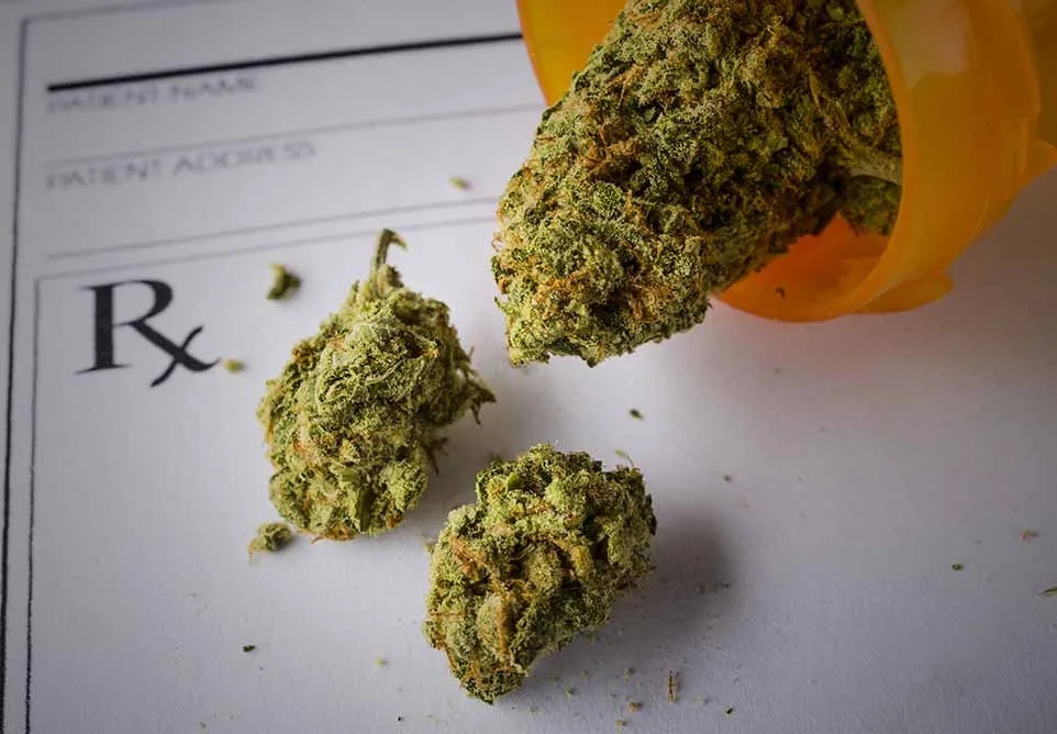 Cannabis buds spilling from an orange prescription bottle onto an Rx prescription pad