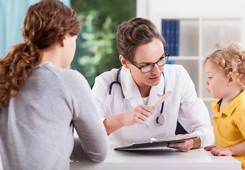Pediatrician with a stethoscope talking with a mother and her young child at a desk in a doctor's office