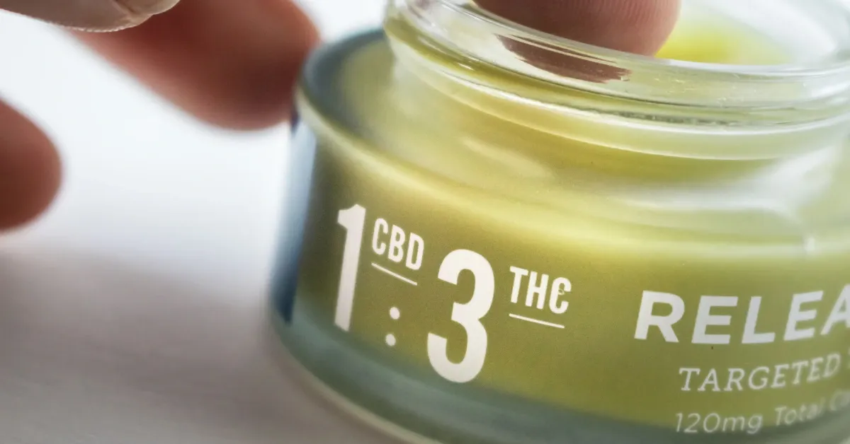 Hand opening a jar of cannabis topical balm labeled with a 1:3 CBD to THC ratio