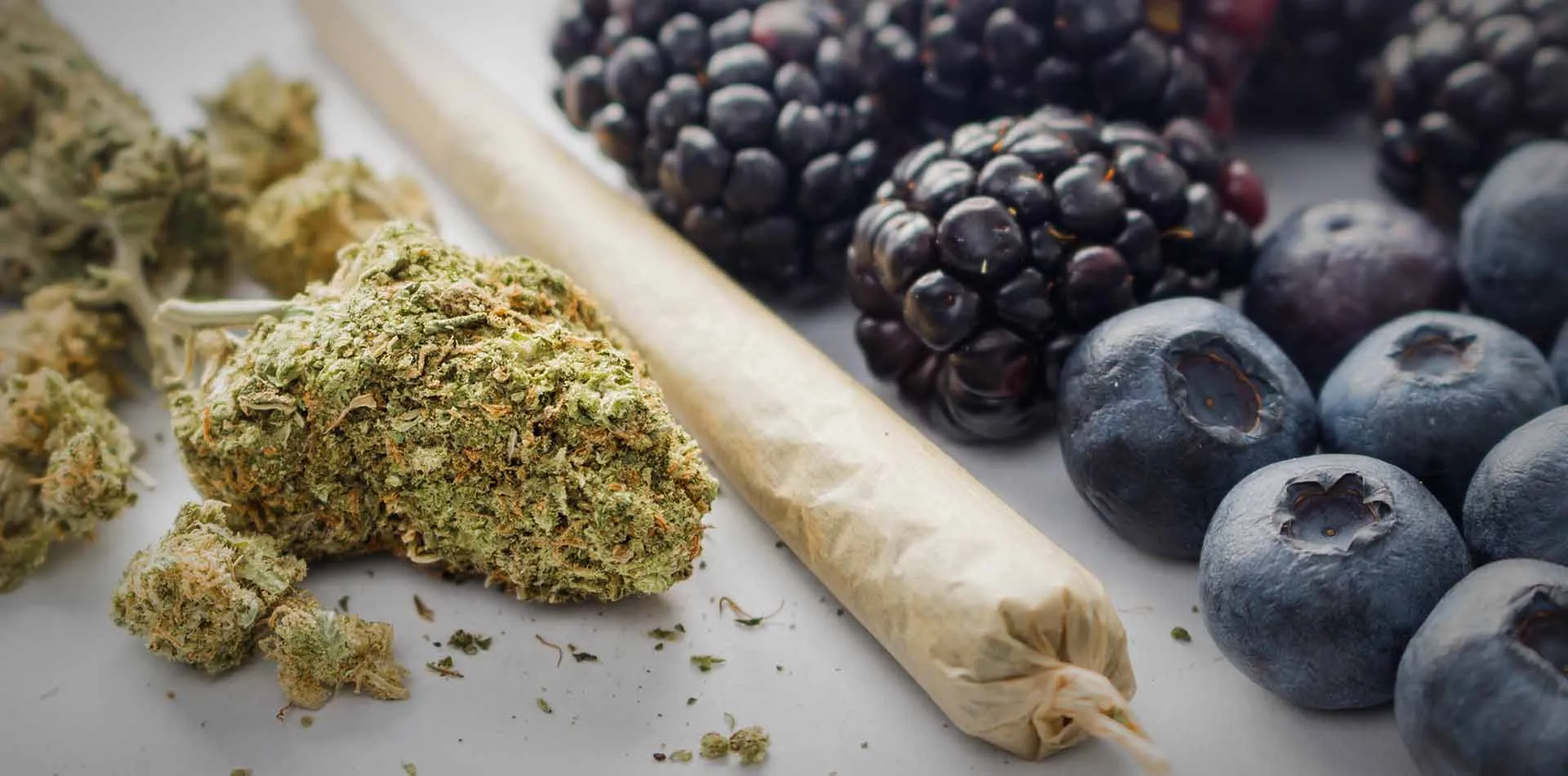 Cannabis flower and a rolled joint beside fresh blueberries and blackberries