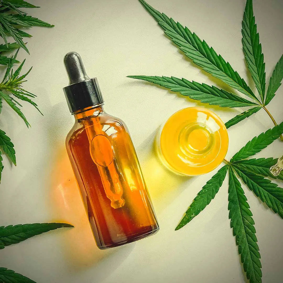 Amber dropper bottle of cannabis oil next to a dish of golden oil and cannabis leaves
