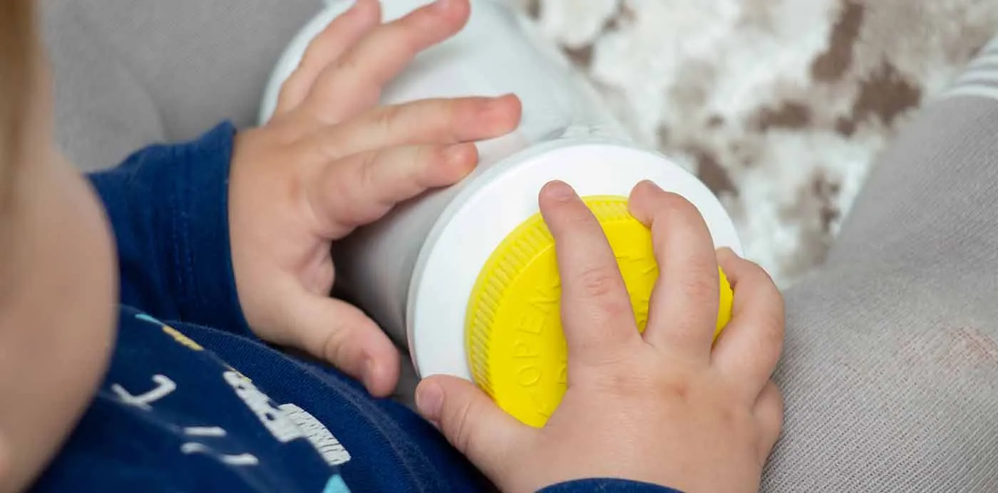 Toddler’s hands gripping a white container with a yellow child-resistant lid