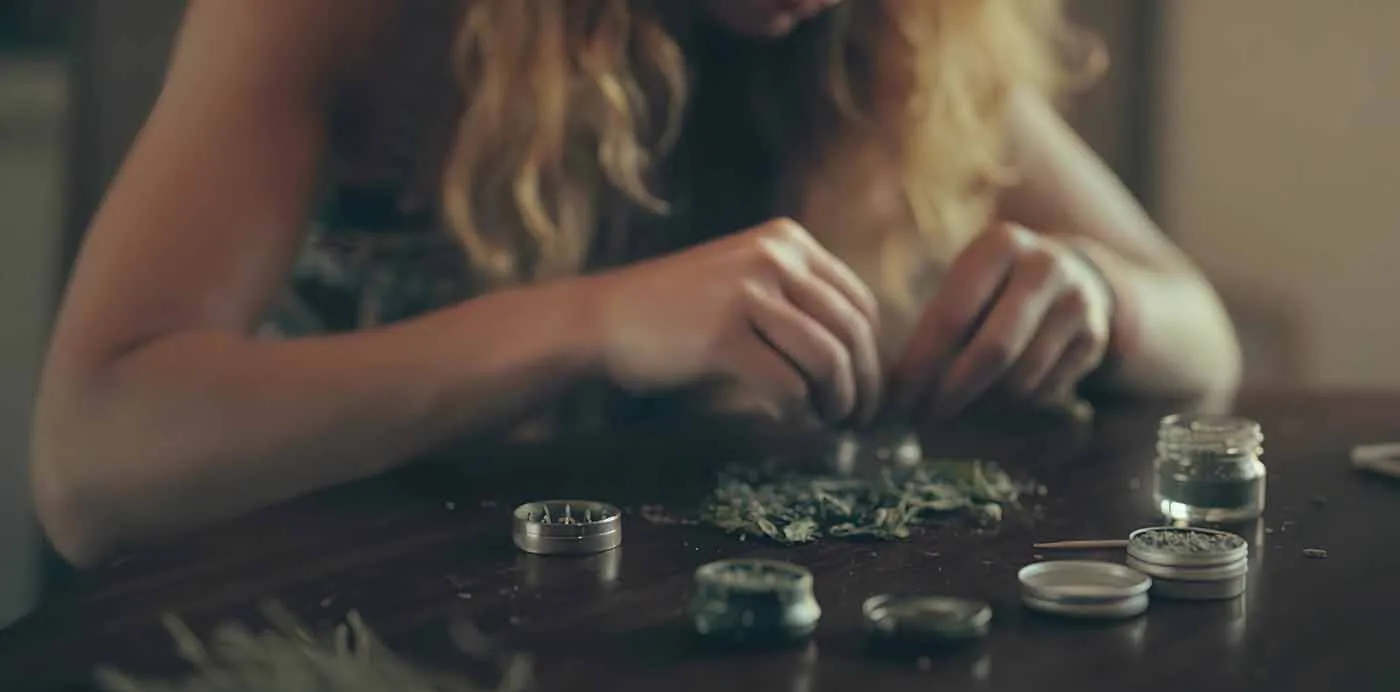 Woman blending cannabis strains from small jars on a table