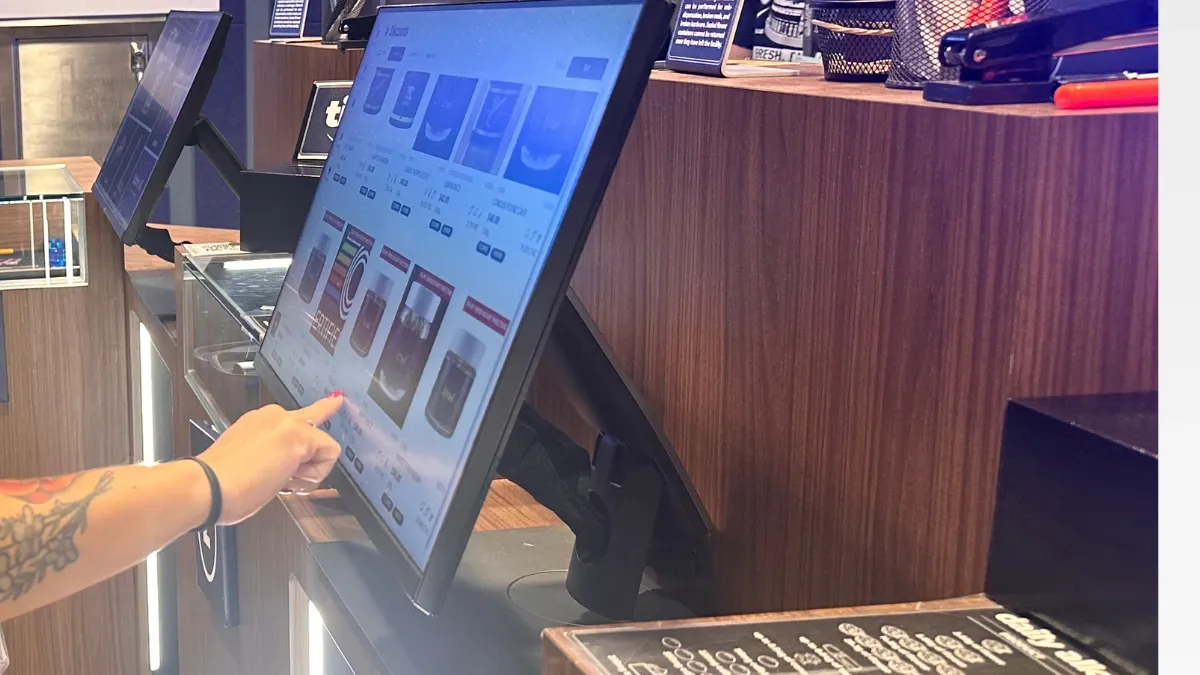 Customer browsing cannabis products on a touchscreen menu kiosk at a Bloom dispensary counter