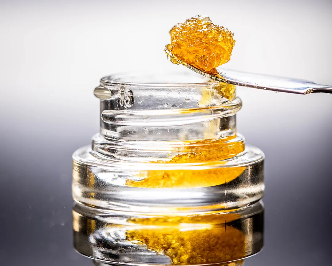 Golden cannabis concentrate scooped onto a metal dab tool above an open glass jar of concentrate