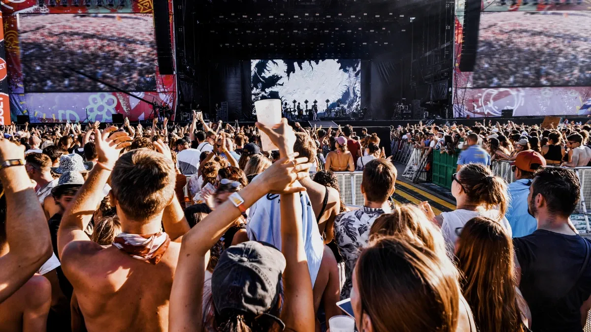 Crowd with raised hands at a daytime outdoor music festival in front of the main stage