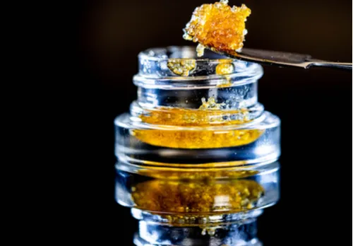 Dab tool lifting a piece of golden honeycomb cannabis concentrate above a small glass jar