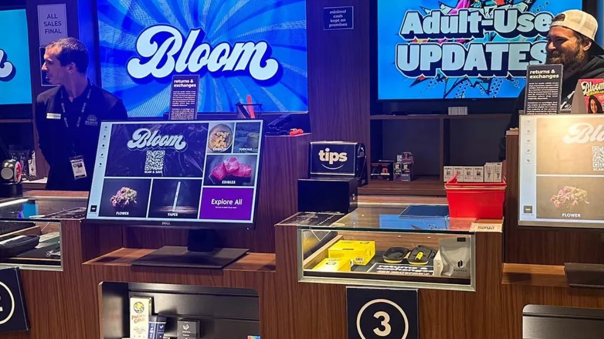 Bloom budtender at the sales counter of an Ohio dispensary, ready to help a customer, with Bloom menu screens behind.