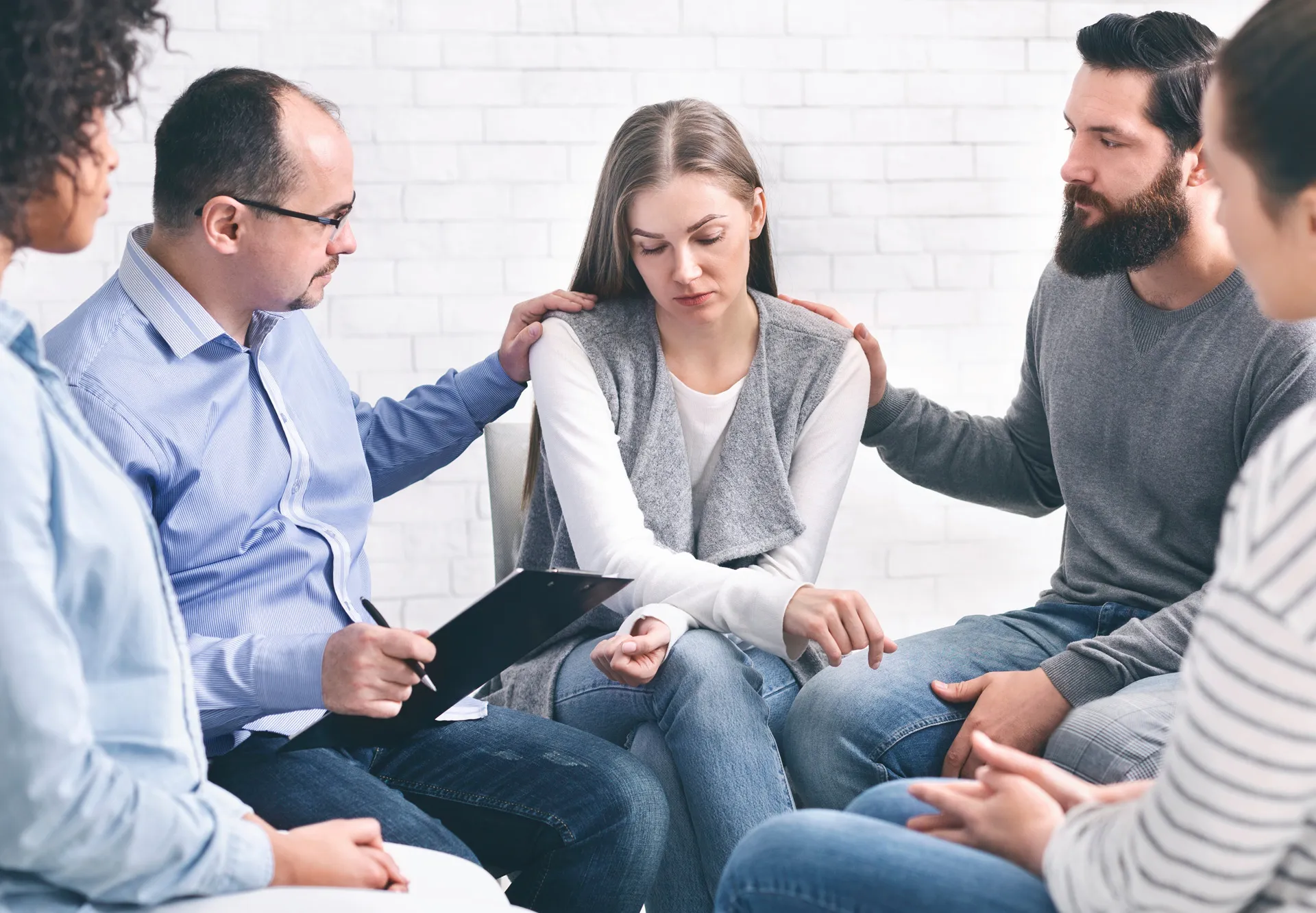 Young woman being comforted by others sitting in a circle during a group therapy session