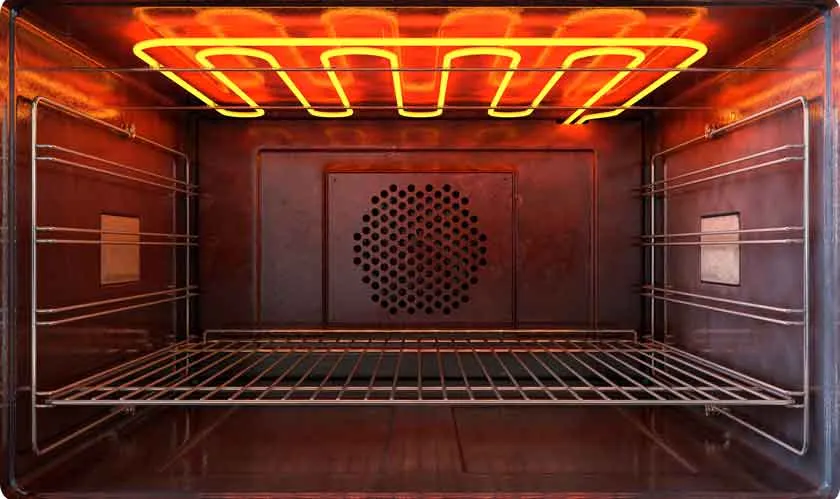 Inside of an empty oven with glowing red heating elements above a wire rack