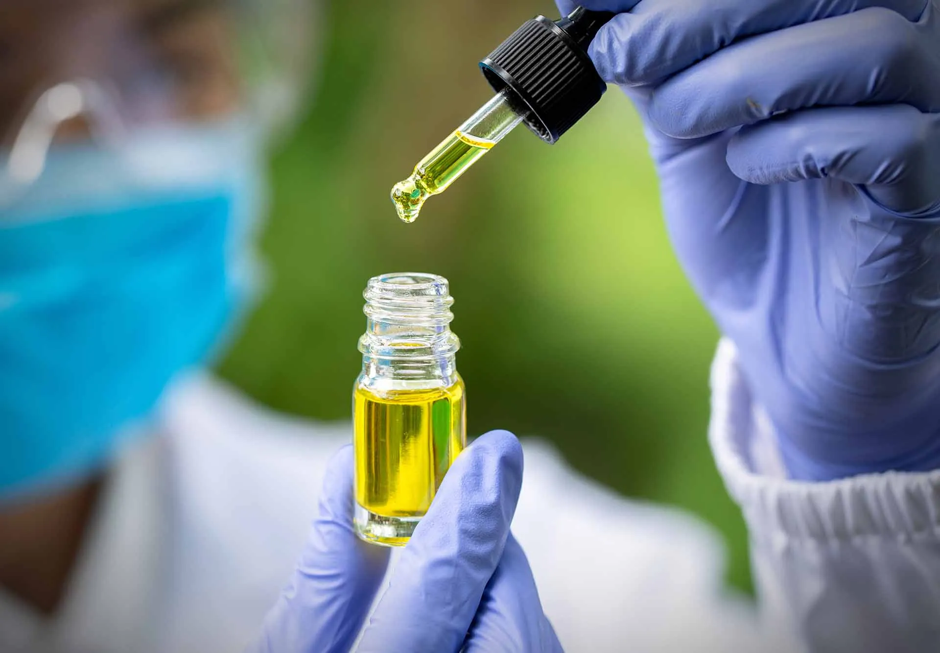 Gloved hands filling a dropper from a small bottle of CBD oil in a lab