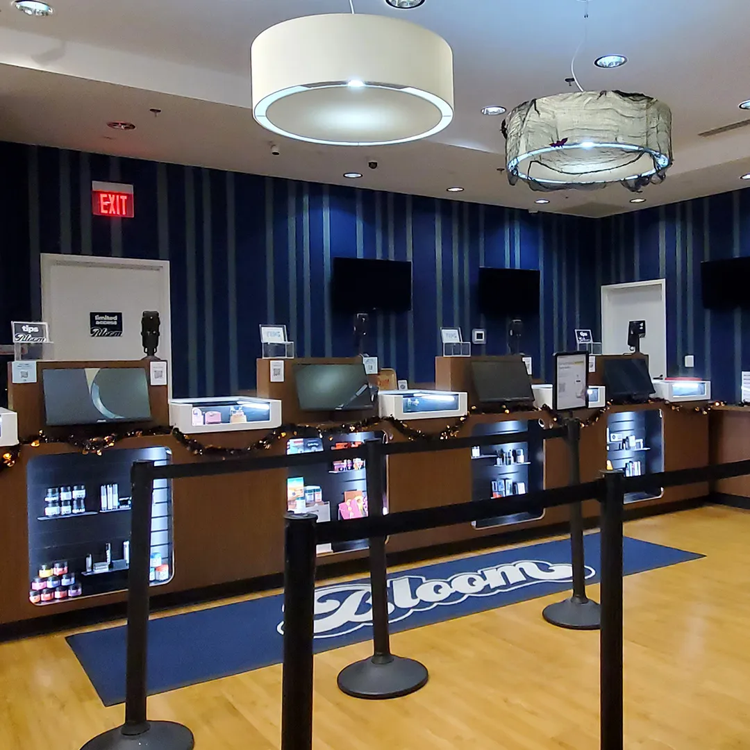 Sales counter at the Bloom Germantown dispensary in Maryland, with service stations, menu screens, queue lanes and a Bloom floor mat.