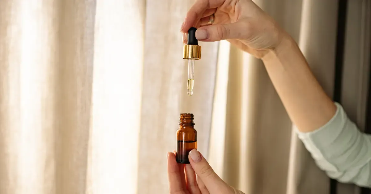 Hand holding a glass tincture bottle while drawing cannabis tincture into a dropper