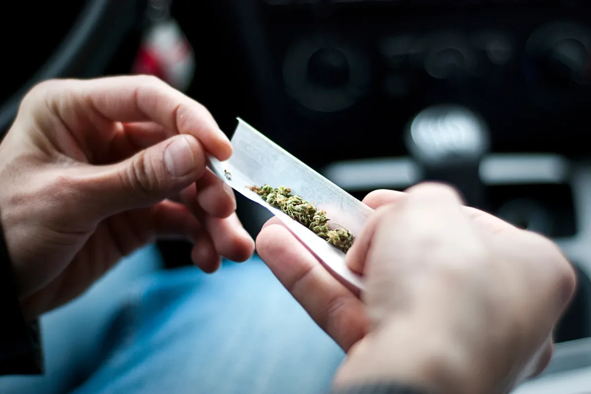 Hands rolling a cannabis joint inside a car — using cannabis in a vehicle is illegal in Ohio for drivers and passengers