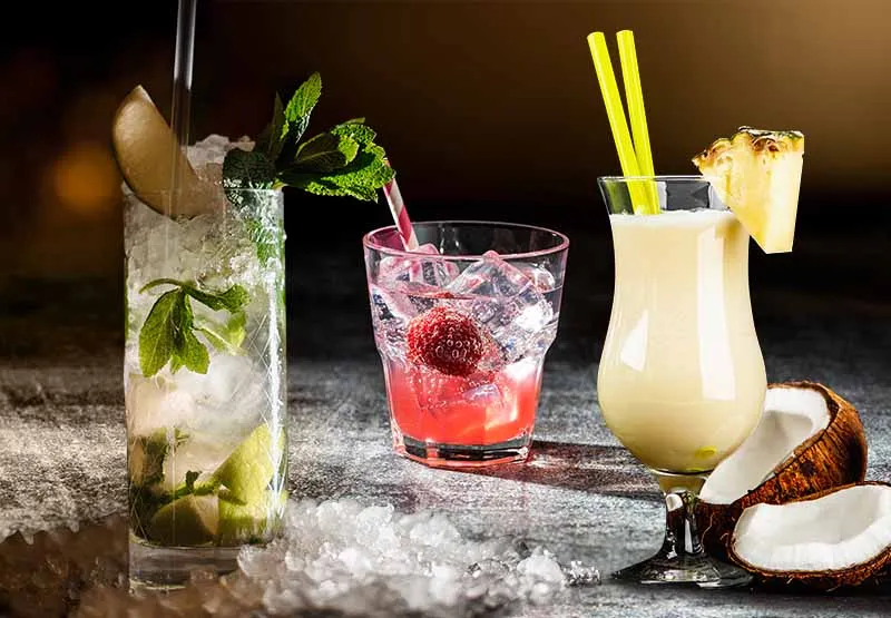 Three colorful mocktail drinks with fruit garnishes on a bar