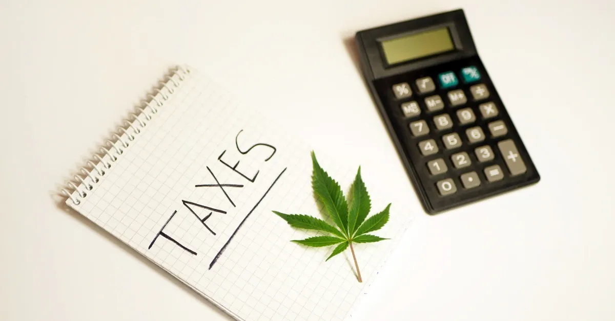 Notepad with the word Taxes written on it, a cannabis leaf and a calculator on a white desk