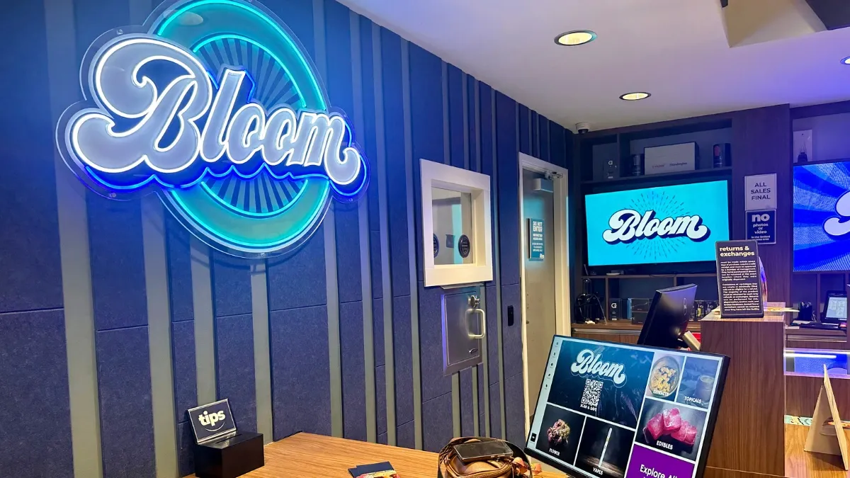 Interior of the Bloom Painesville, Ohio dispensary with a glowing blue Bloom neon sign and display screens
