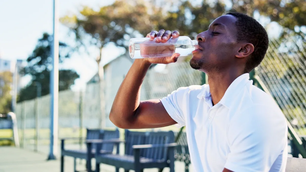 Man drinking from a water bottle while sitting outdoors on a sunny summer day