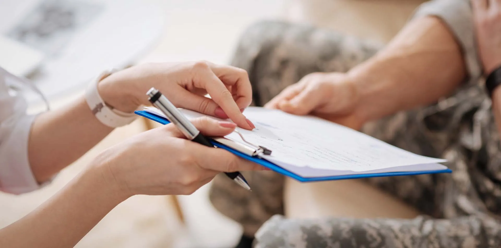 Clinician pointing to a form on a clipboard for a patient in a military uniform