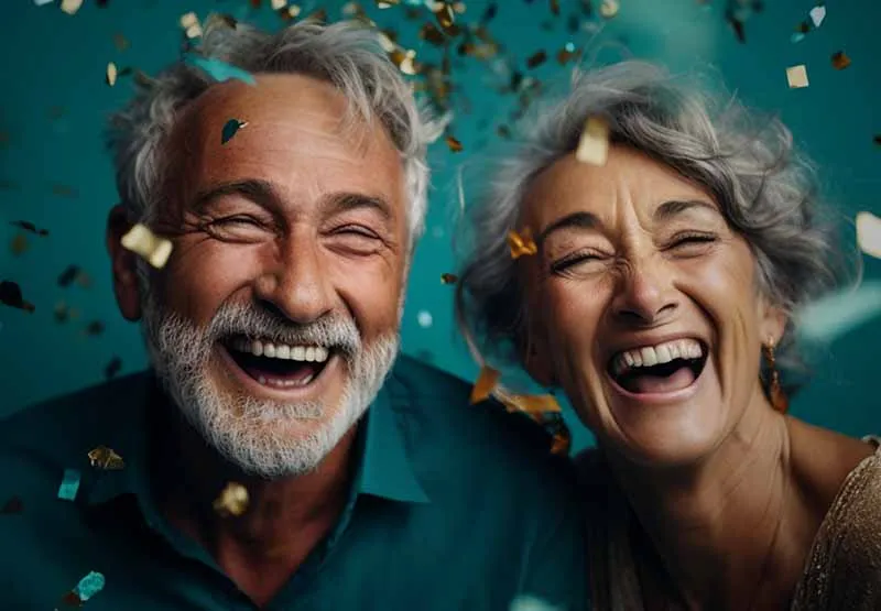Smiling older man with a gray beard and a laughing woman celebrating under falling confetti