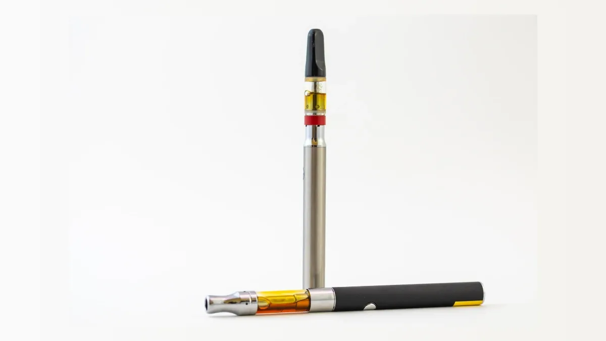 510-thread cannabis vape cartridge attached to a slim vape battery, with a second vape pen lying beside it