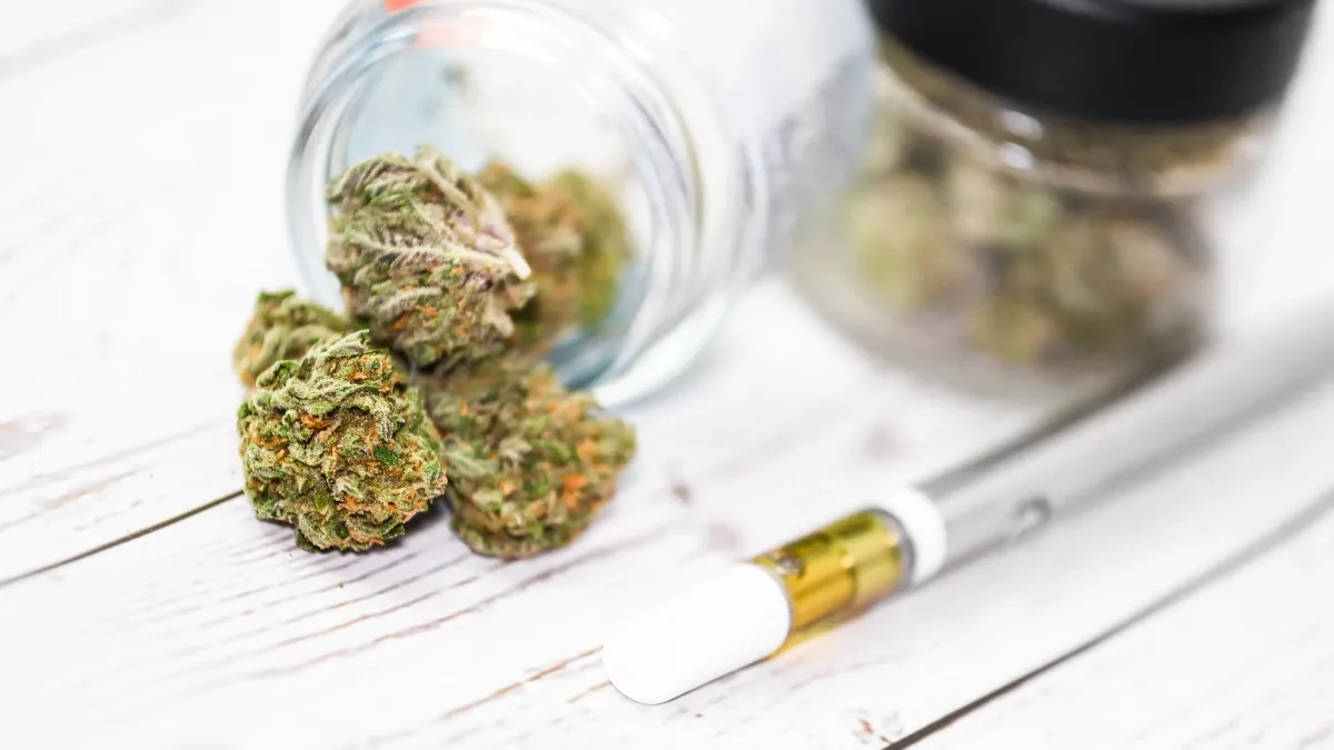 Vape cartridge pen beside a small glass jar of cannabis flower buds
