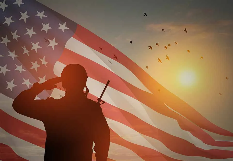 Silhouette of a soldier saluting in front of an American flag at sunset