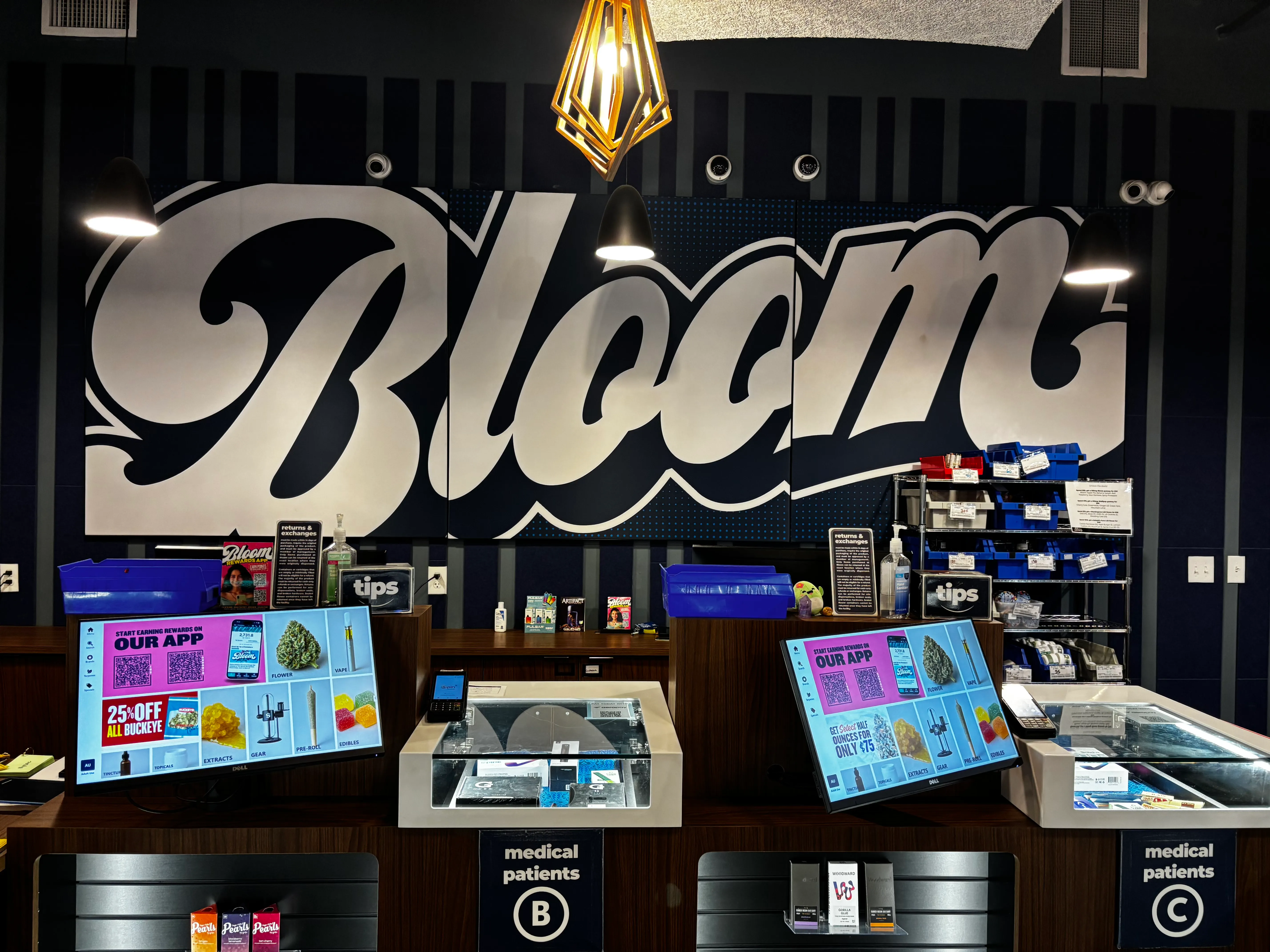 Sales counter at the Bloom dispensary in West Columbus, Ohio, with menu screens beneath a large Bloom script mural.