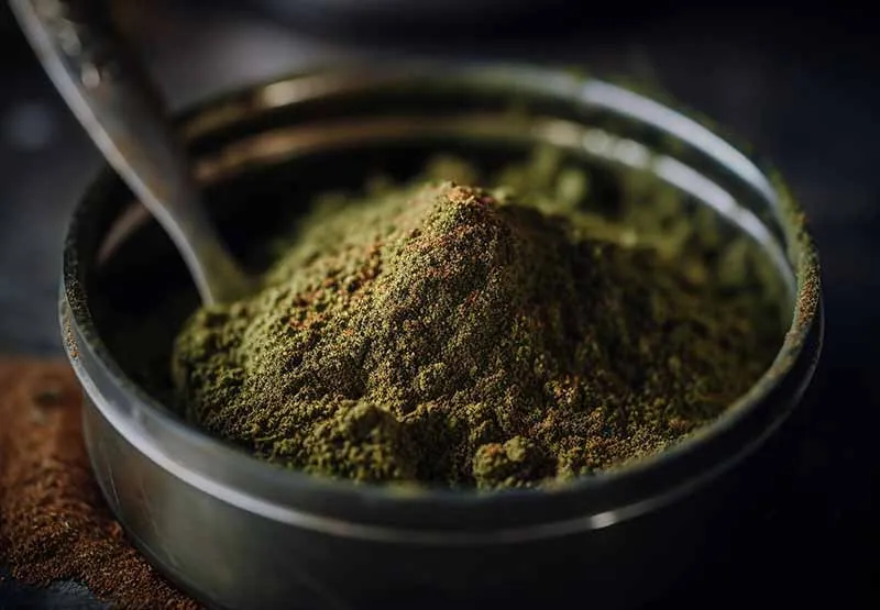 Spoon resting in a metal grinder chamber filled with fine green kief powder