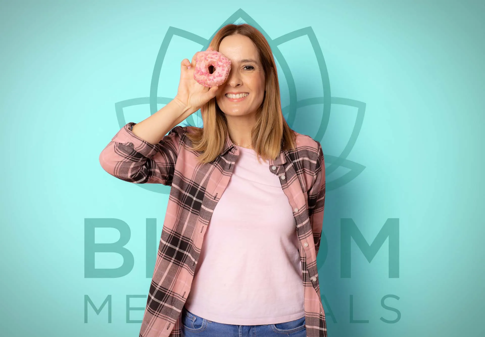 Smiling woman holding a pink frosted donut over one eye in front of a teal Bloom logo backdrop